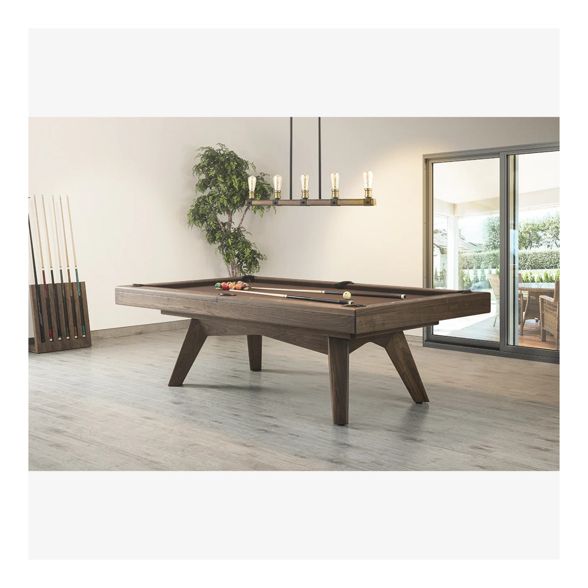 Wooden pool table in a modern living room with a plant and chandelier in the background.