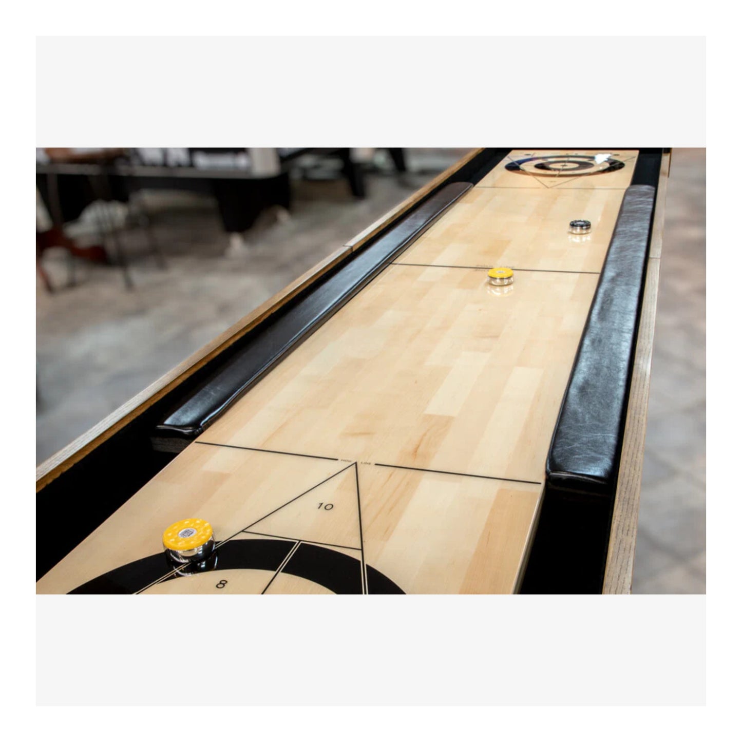 A close-up of the end of the shuffleboard's laminated playing surface, showing the built-in abacus score counter on the brown cabinet.
