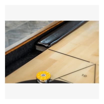 Yellow shuffleboard puck (rock) on the smooth, laminated playing surface, ready for a game.