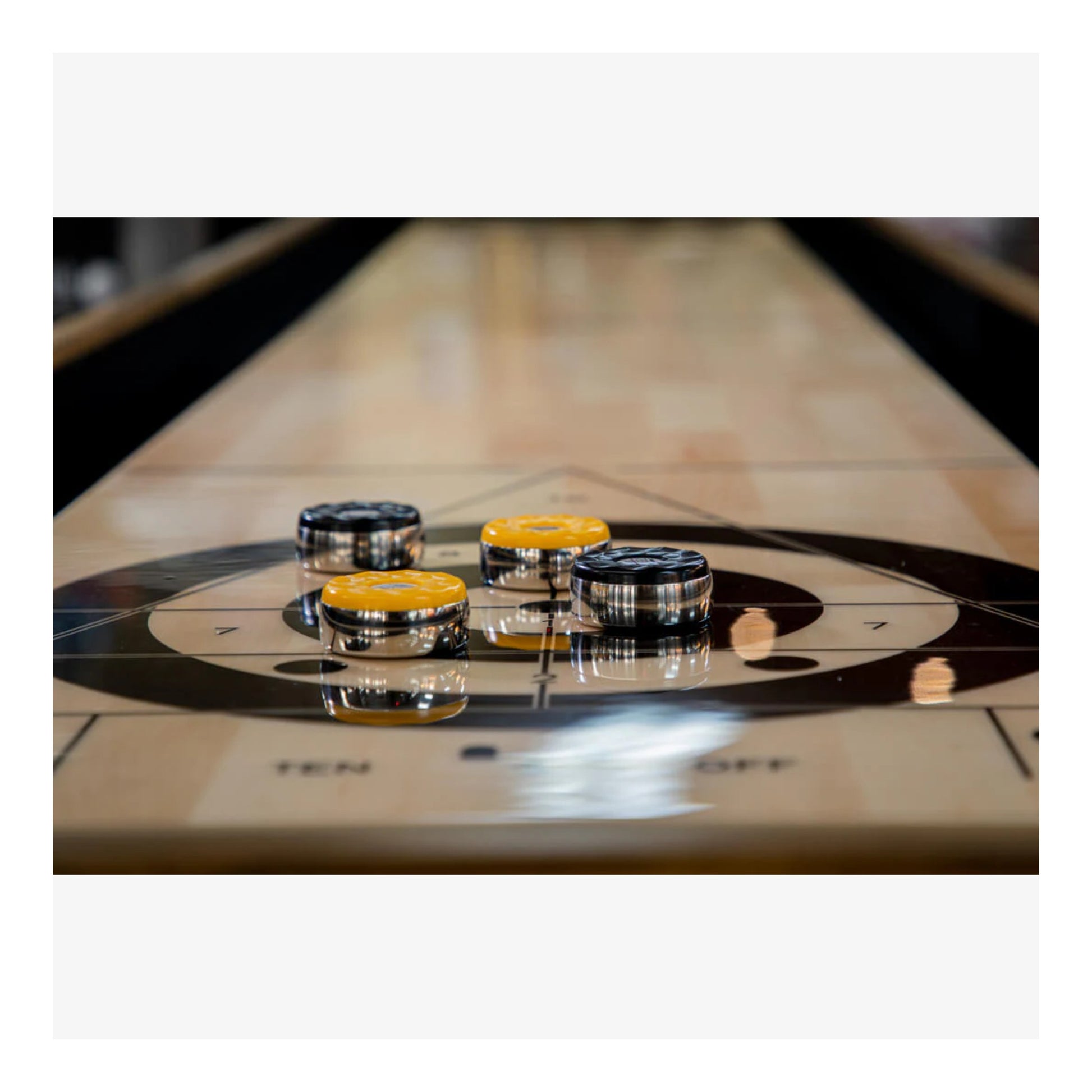 Black and yellow shuffleboard pucks (rocks) on the smooth, laminated playing surface, ready for a game.