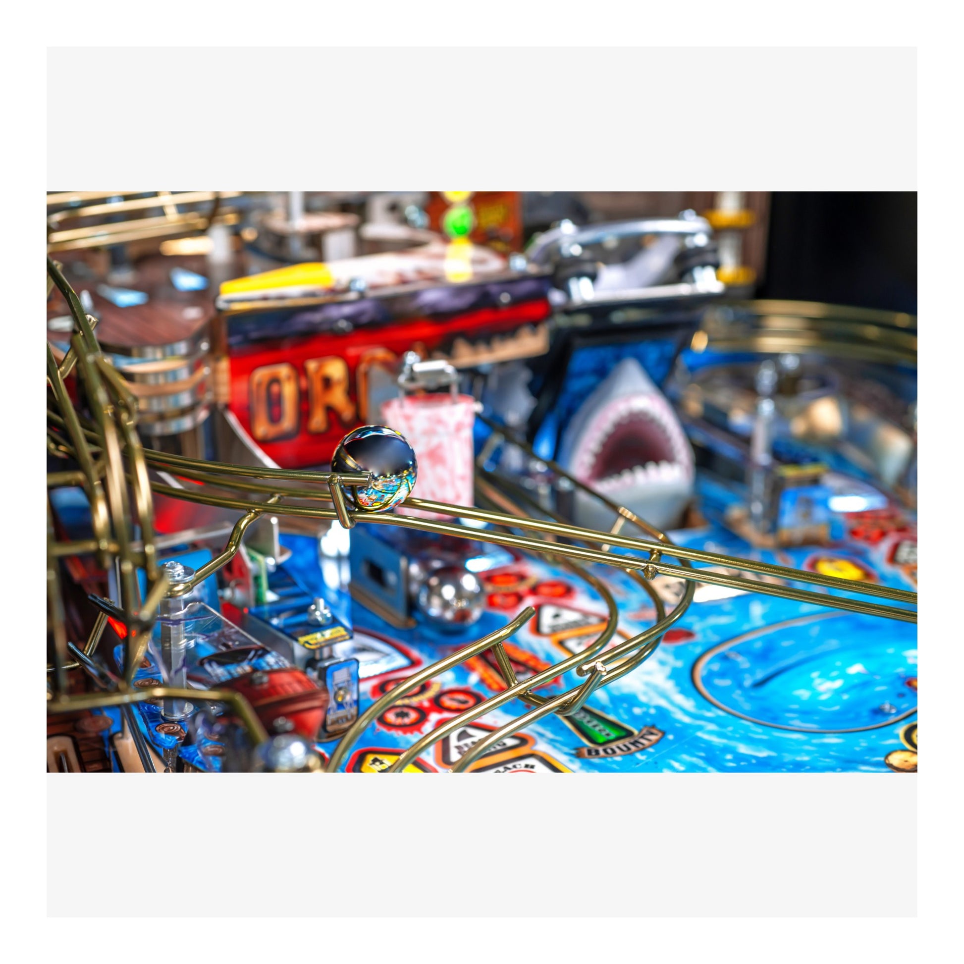 Close-up of a pinball machine with a shark design and colorful playfield.