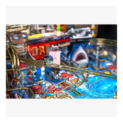 Close-up of a pinball machine with a shark design and colorful playfield.