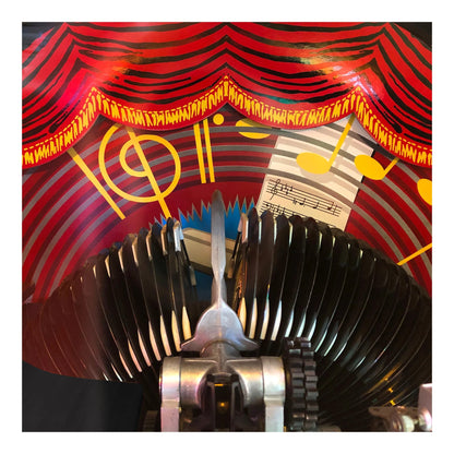 Close-up of a mechanical music box with gears and a red curtain background.