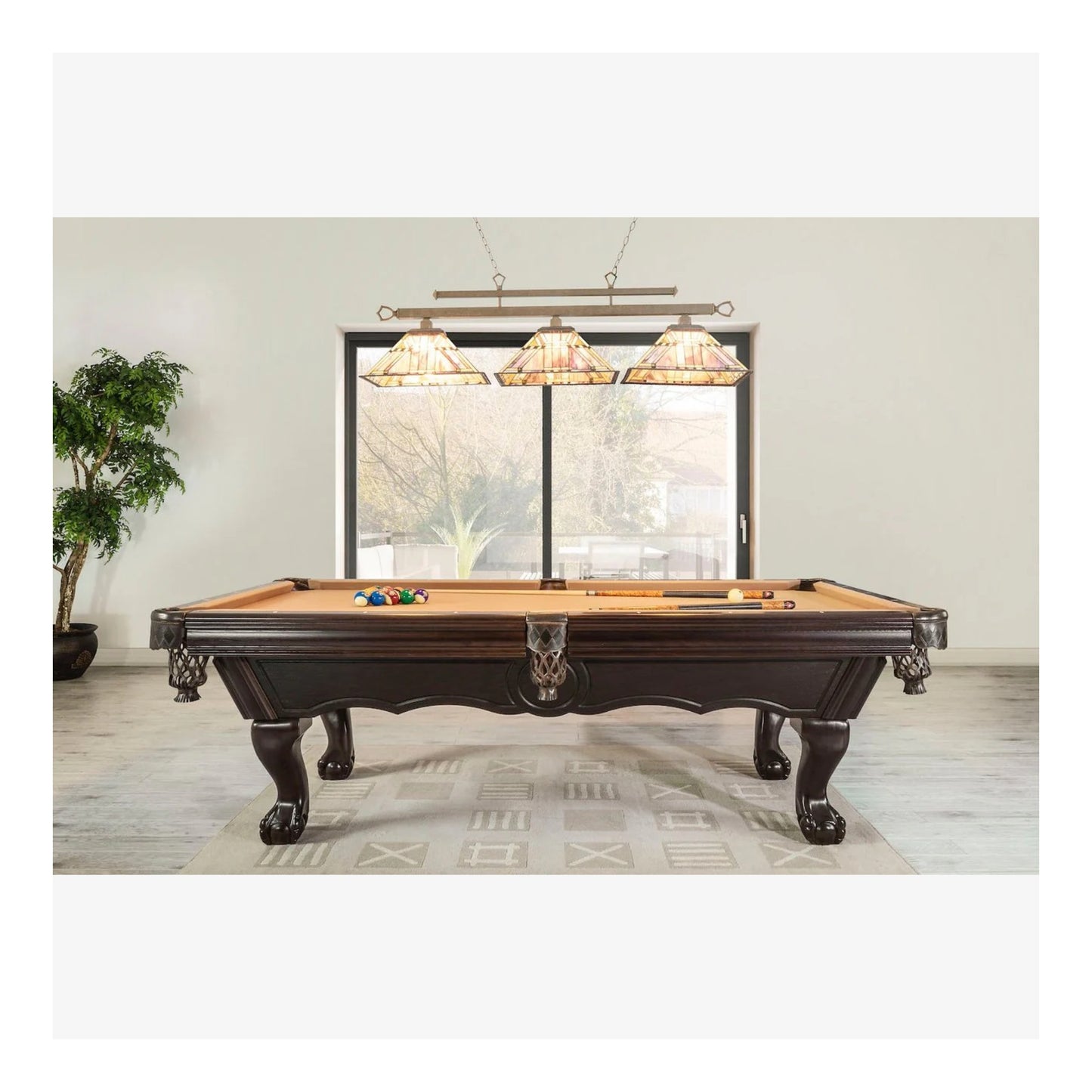 Wooden pool table with cues and balls in a room with large windows and decorative lamps.