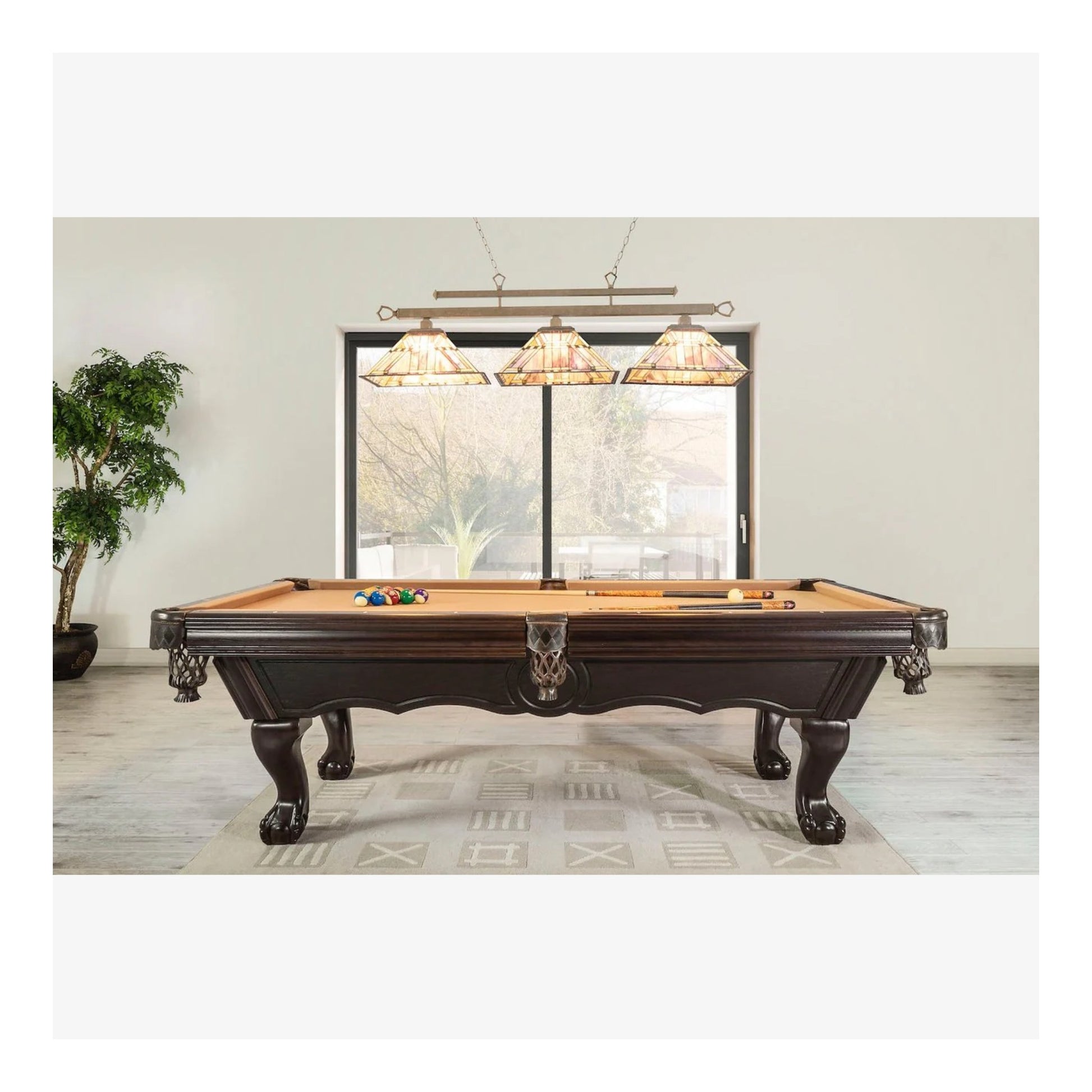 Wooden pool table with cues and balls in a room with large windows and decorative lamps.