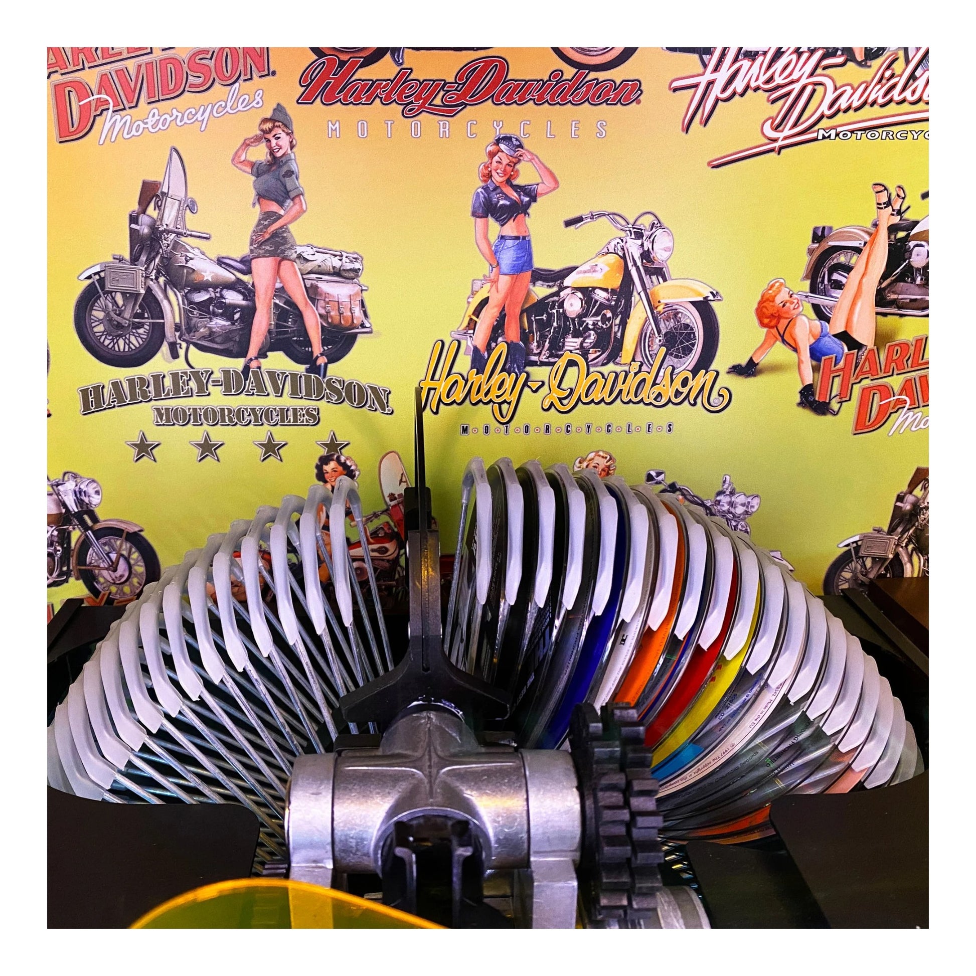 Harley Davidson-themed background with motorcycle and pin-up graphics, featuring a metal exhaust system in the foreground.