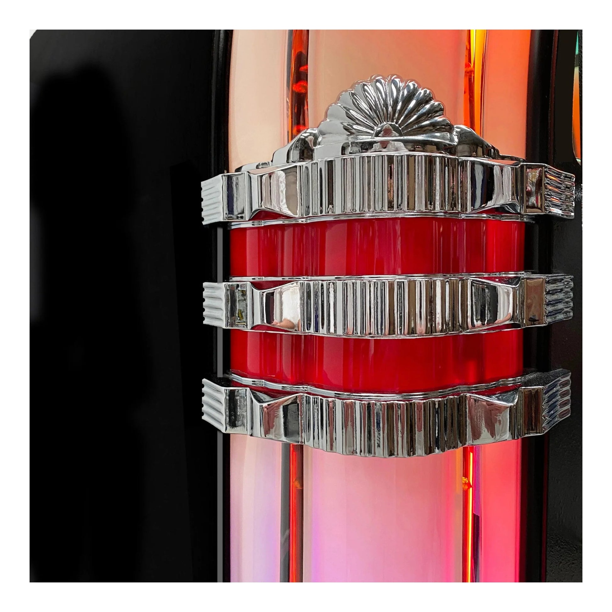 Close-up of a decorative object with red central section and silver metallic top and bottom sections on a black background.