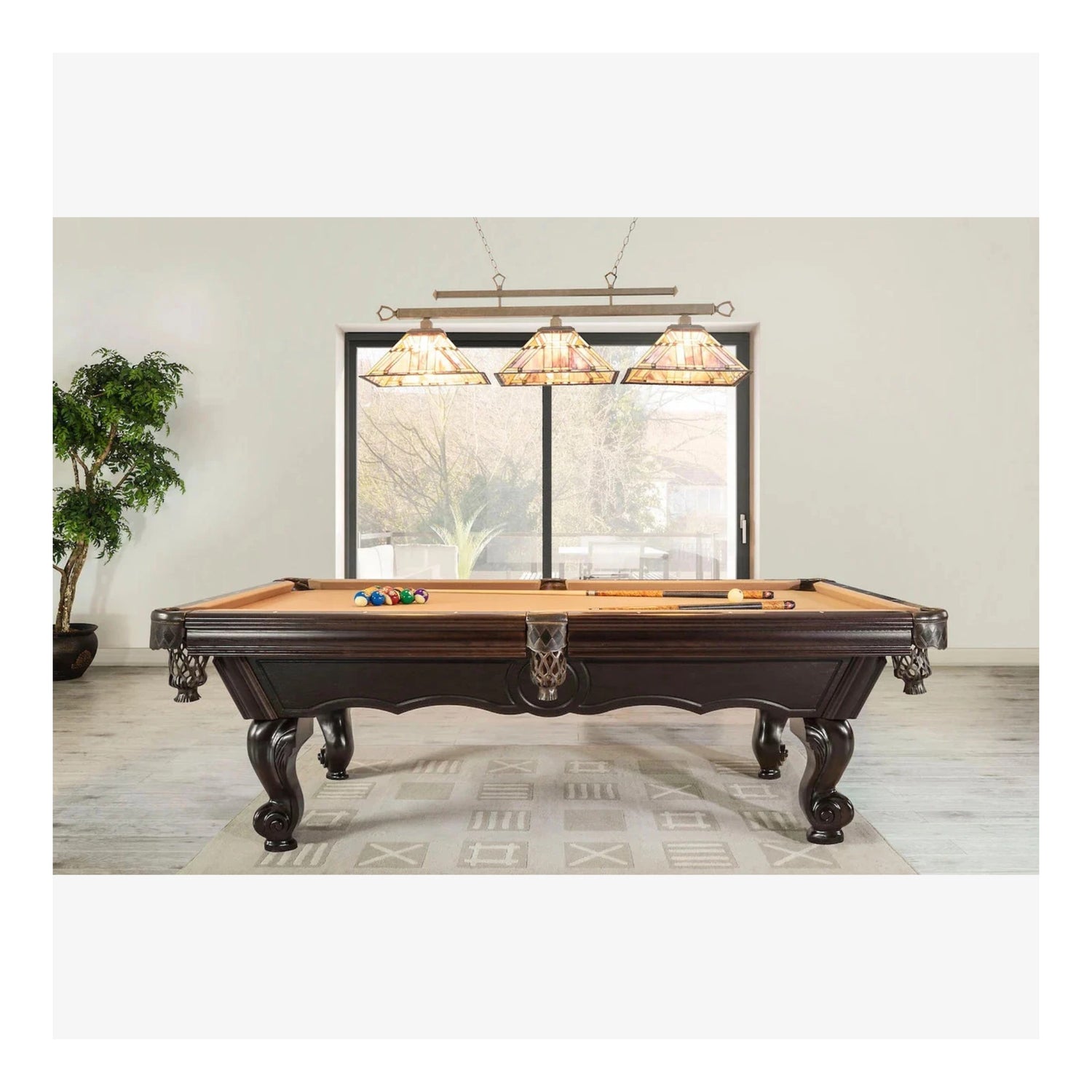 Wooden pool table with cues and balls in a room with large windows and decorative lights.