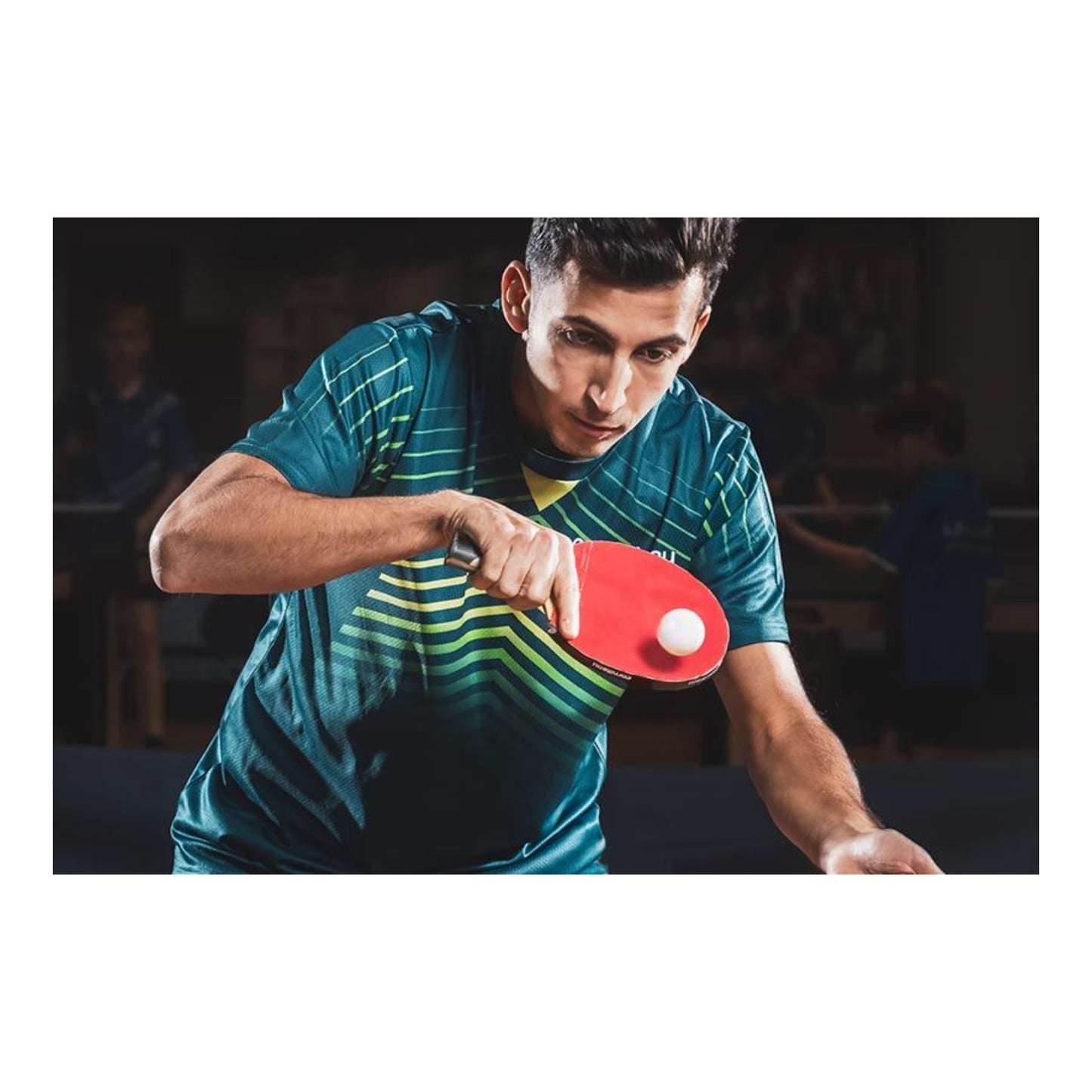 A man playing table tennis, wearing a teal and green striped athletic shirt, holding a red table tennis paddle with a white ball in motion.