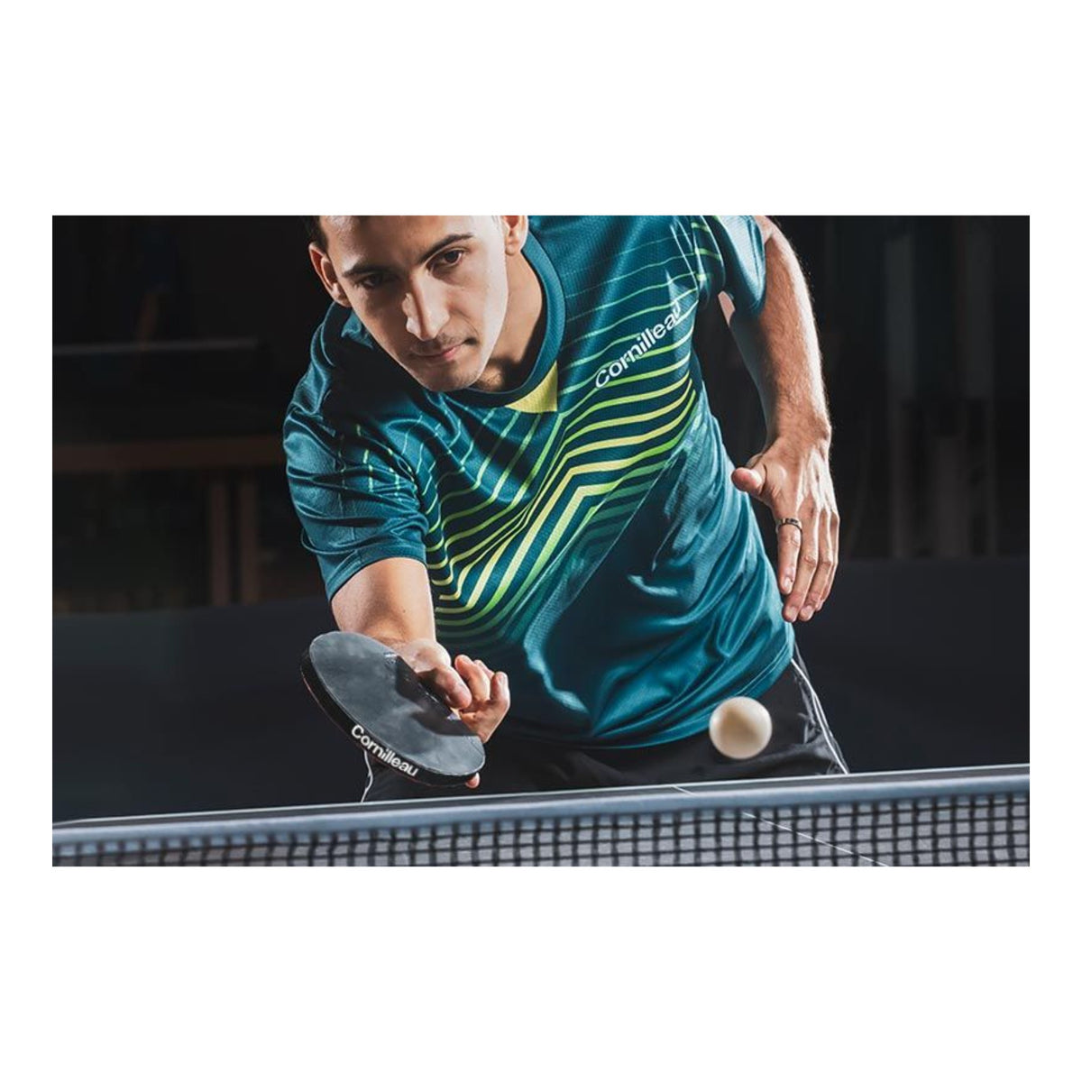 A man playing table tennis, wearing a teal and yellow striped athletic jersey holding a paddle with the Cornilleau logo, with a white table tennis ball in motion.