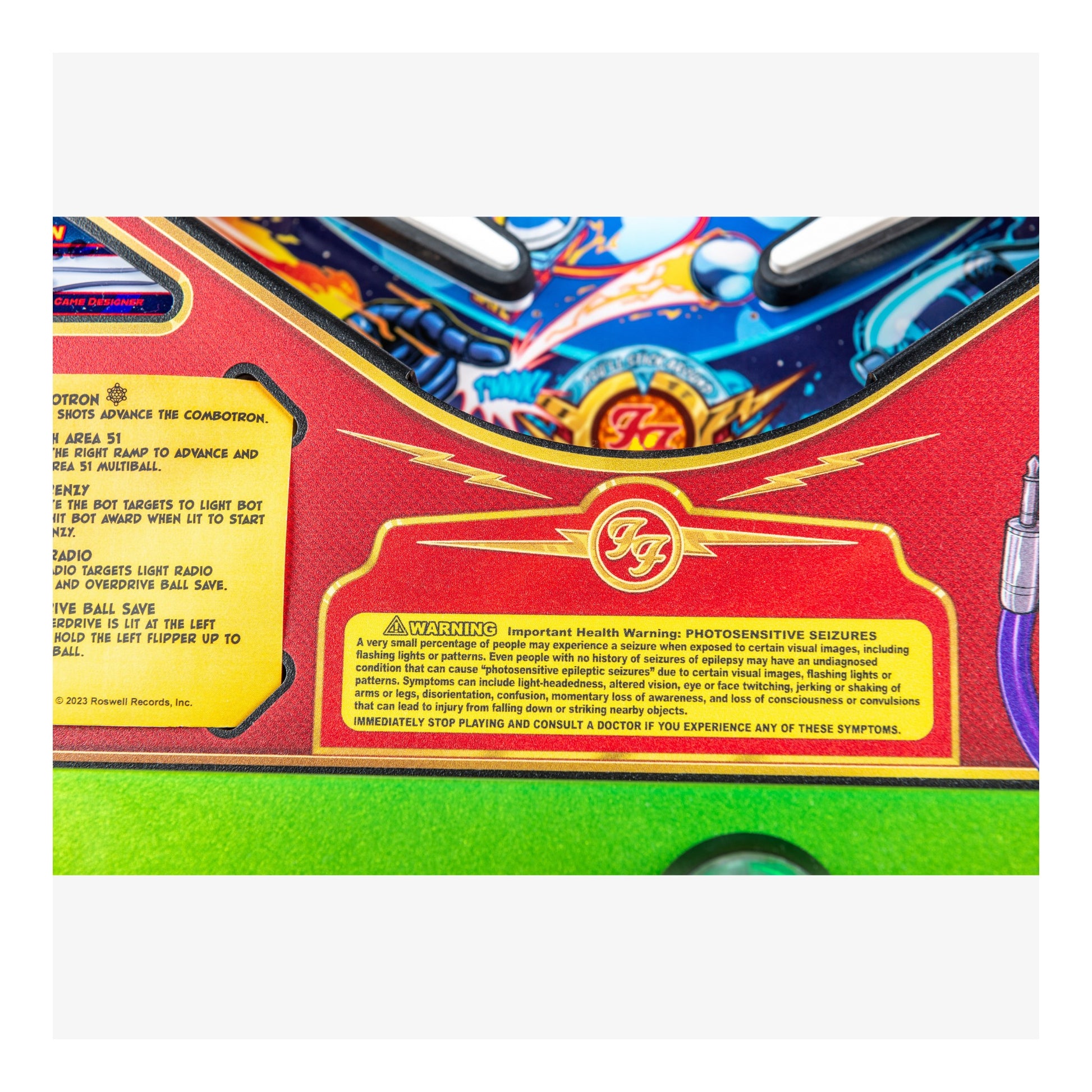 Close-up of a colorful pinball machine with a warning label on a white background
