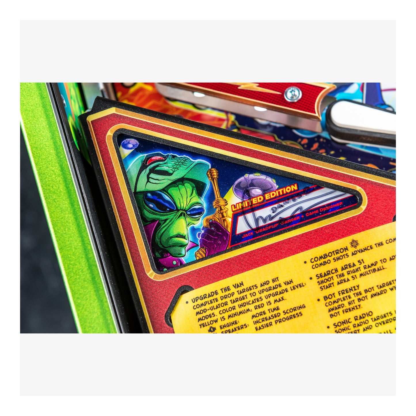 Close-up of a colorful pinball machine with an alien graphic and text on a white background
