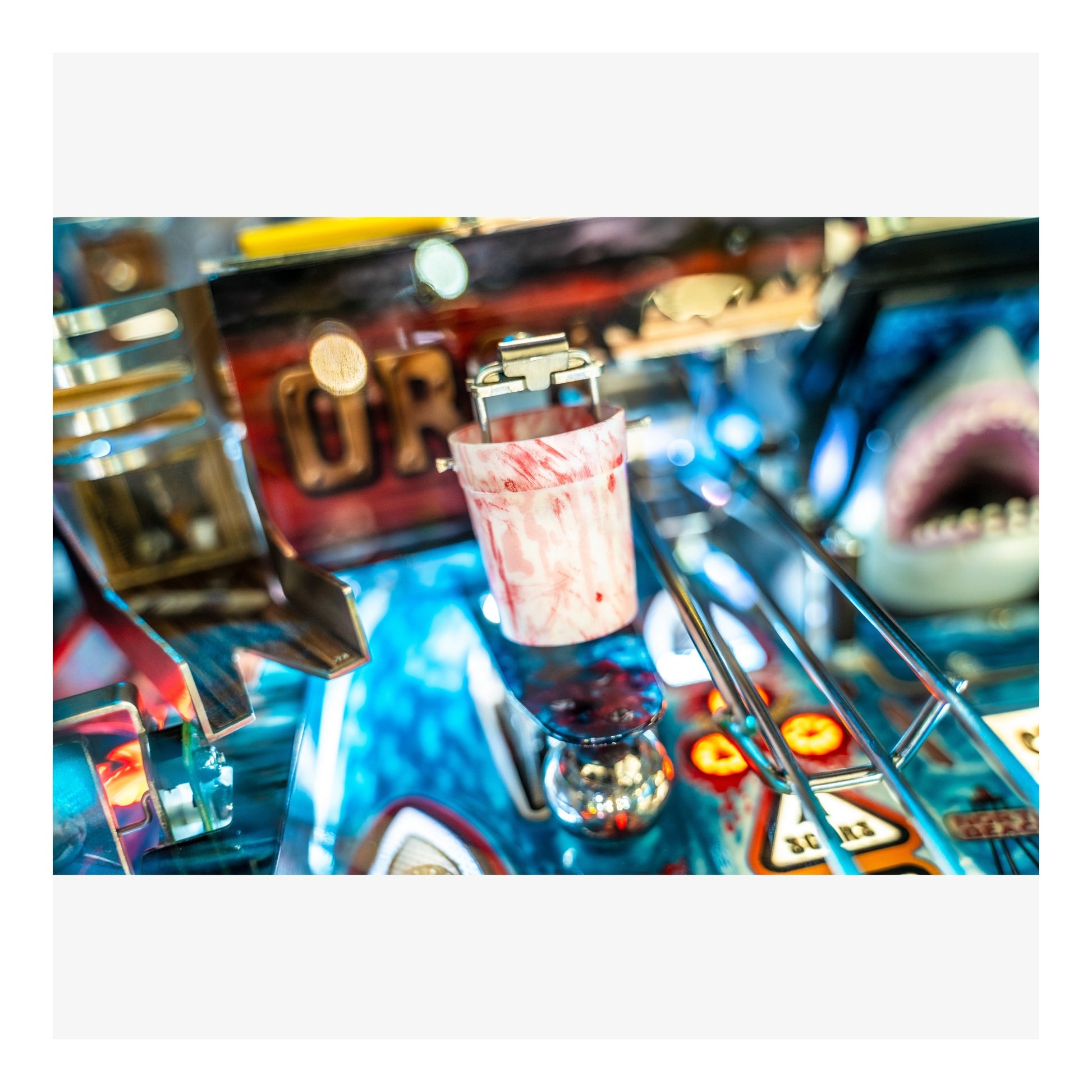 Close-up of a pinball machine with a glass of pink liquid on the playfield.