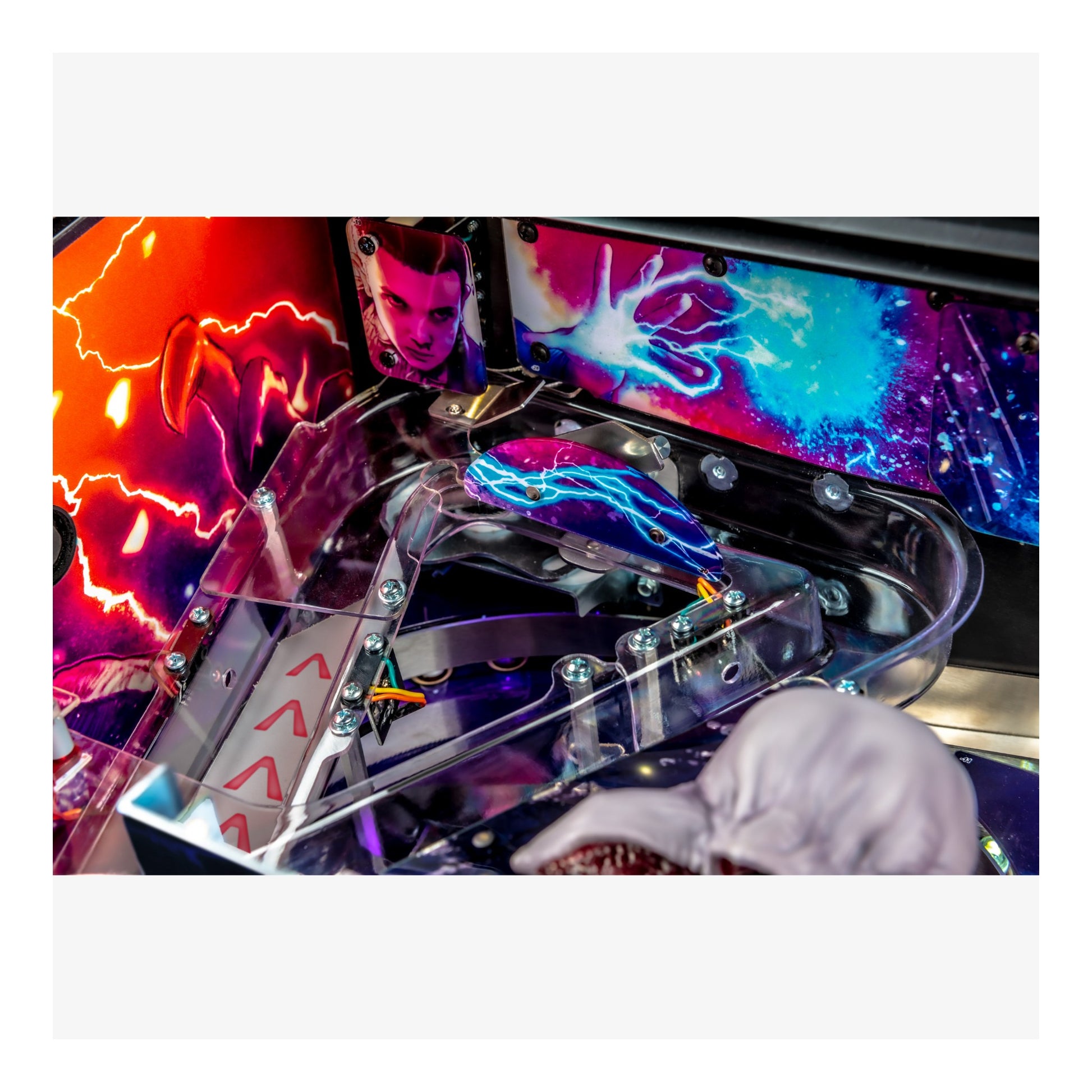 Close-up of a colorful pinball machine with vibrant graphics and a hand interacting with it.