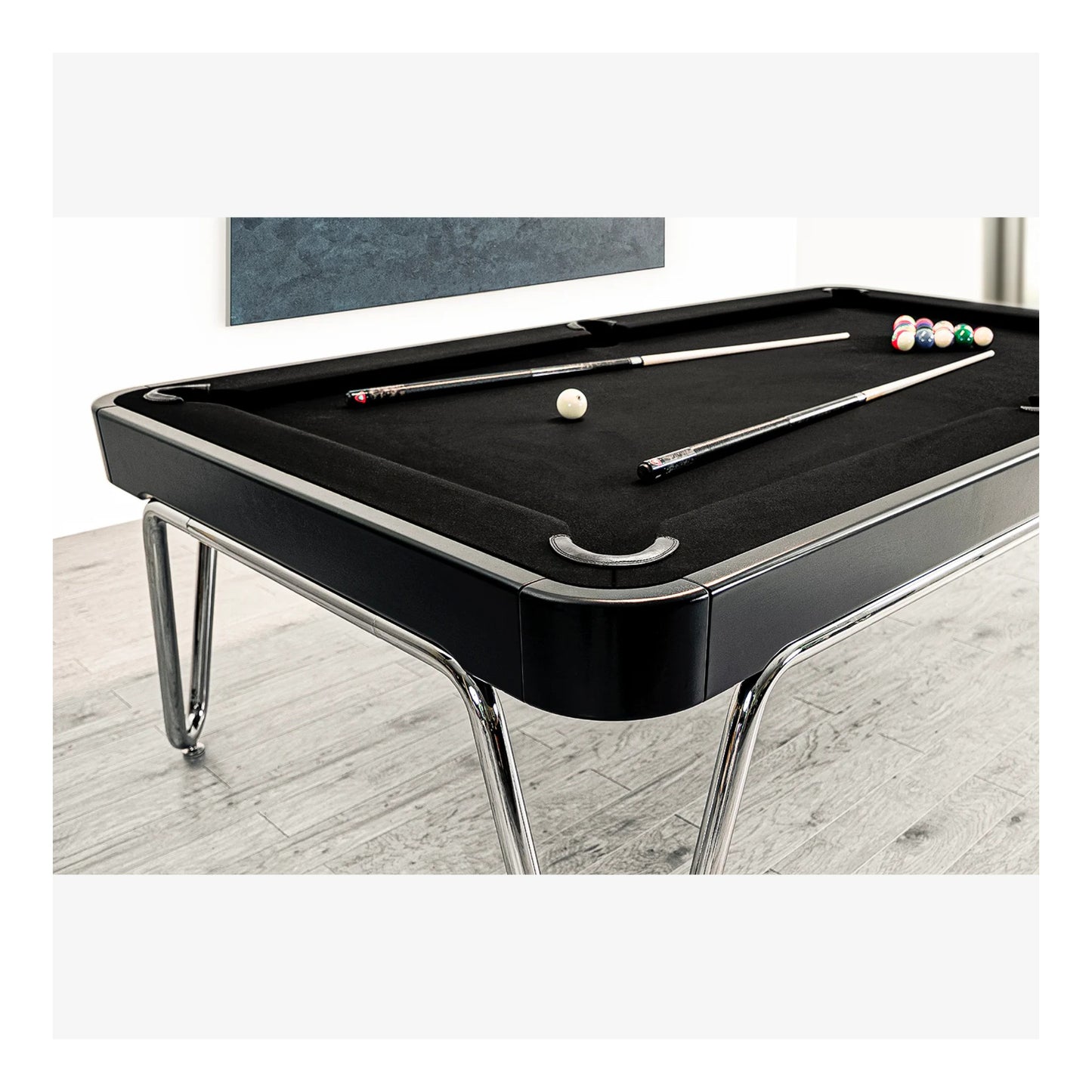 Black pool table with pool cues and balls on a light wood floor.
