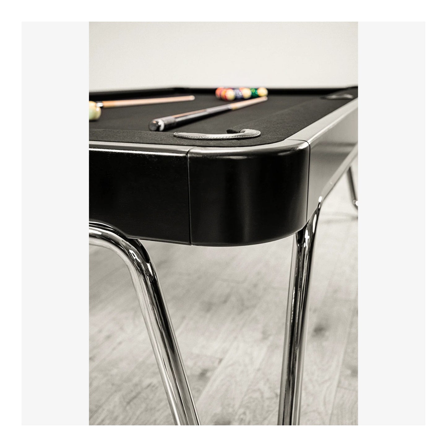 Black pool table with cues on a light wood floor