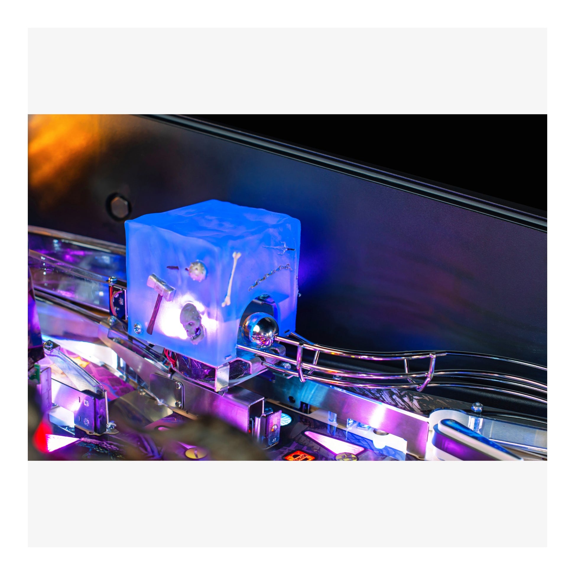 Close-up of a pinball machine with a blue cube and metallic components.