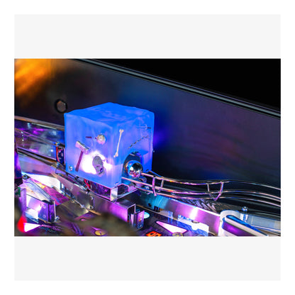 Close-up of a pinball machine with a blue cube and metallic components.