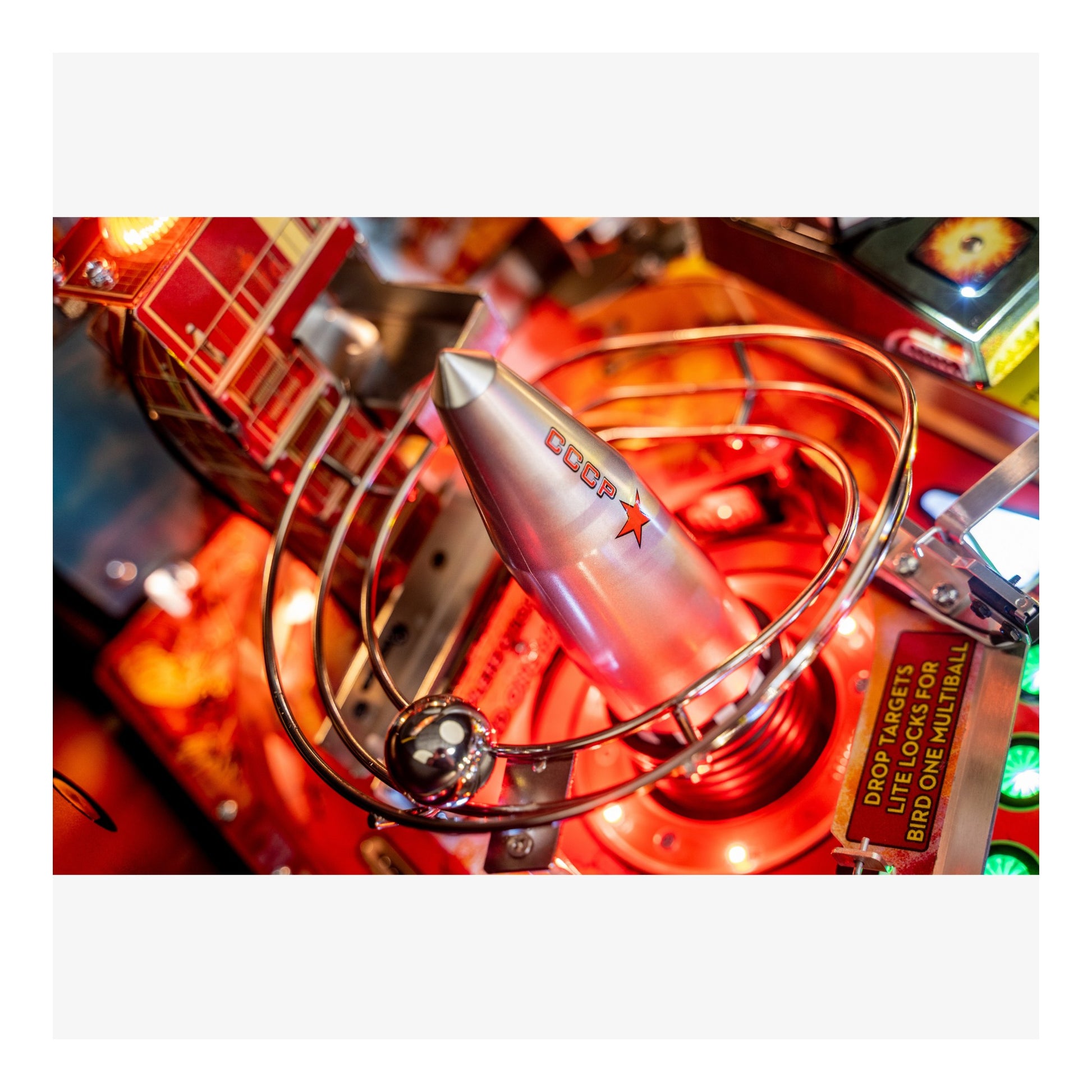 Close-up of a pinball machine with a glowing red light and metallic components.