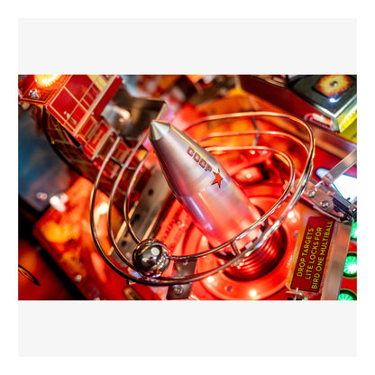 Close-up of a pinball machine with a glowing red light and metallic components.