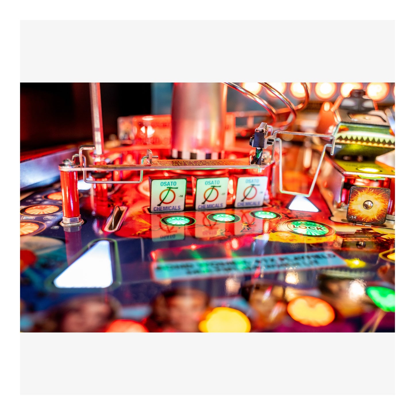 Close-up of a pinball machine with colorful lights and players in the background
