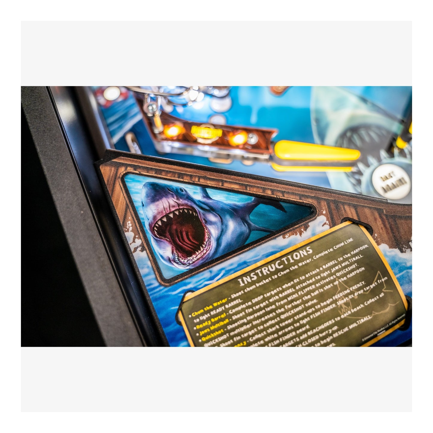 Close-up of a pinball machine with a shark artwork and instructions panel.