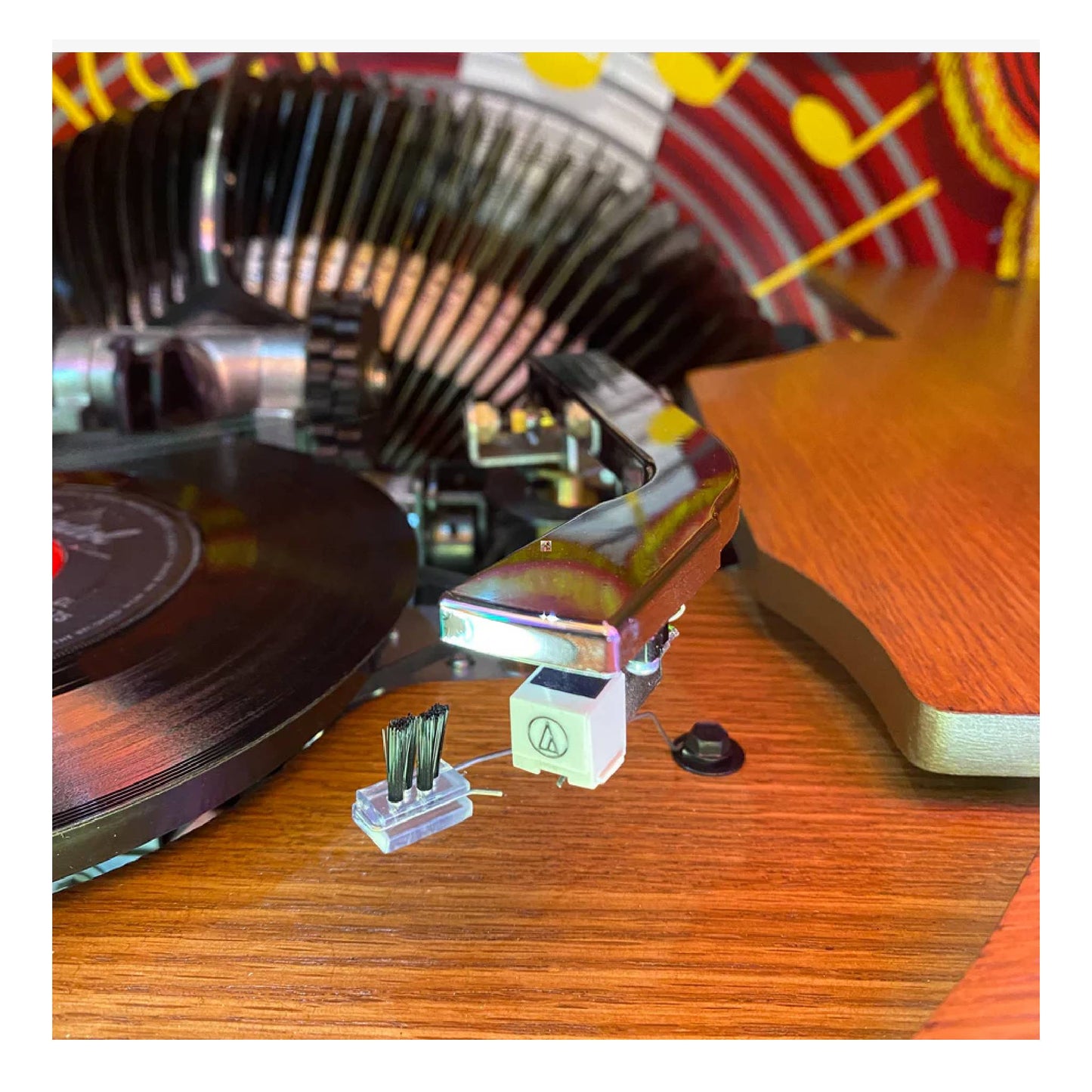 Close-up of a vinyl record player headshell with a cartridge on a wooden turntable.
