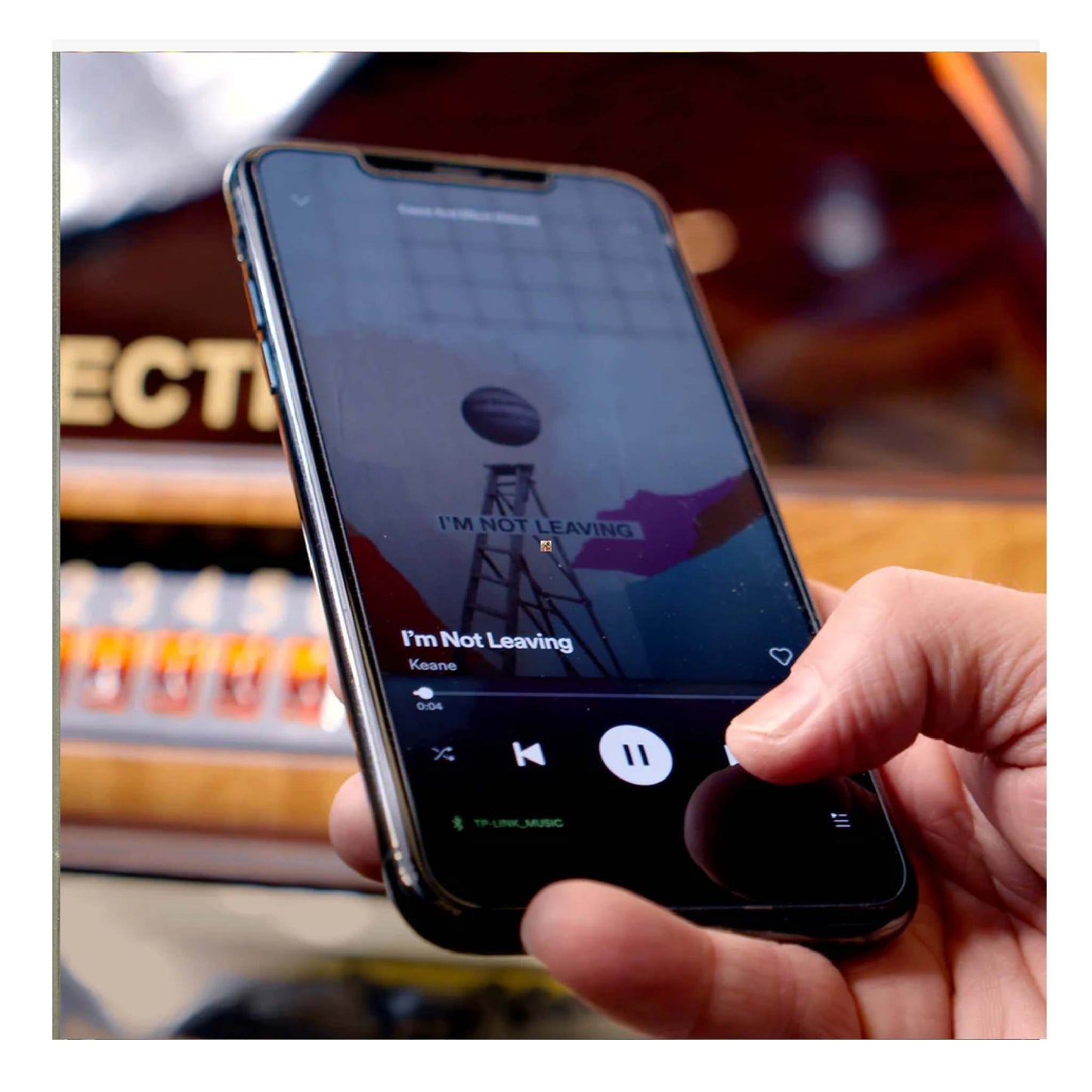 Hand holding a smartphone with a music app playing 'I'm Not Leaving' by Kehlani.