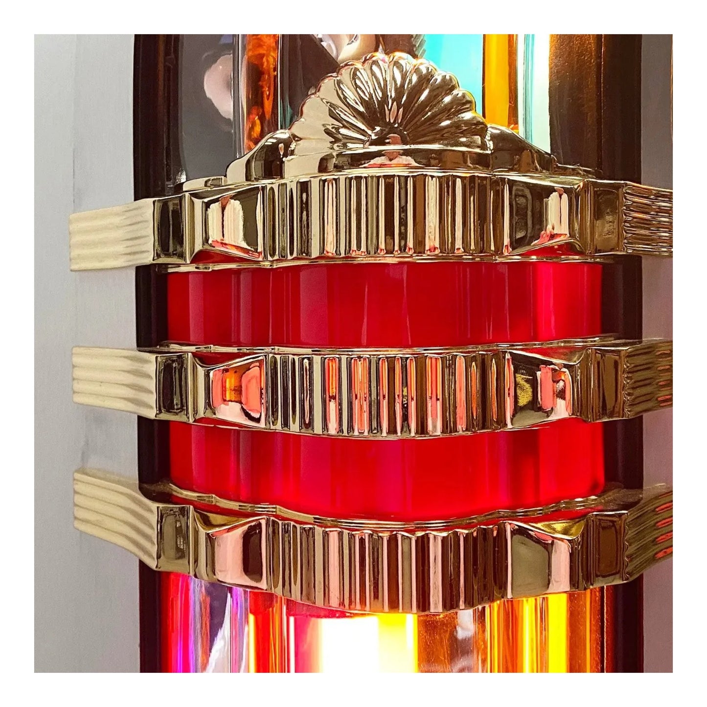 Close-up of a red glass object with gold metal bands against a colorful background