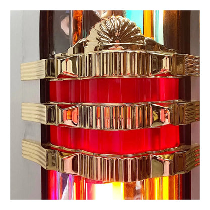 Close-up of a red glass object with gold metal bands against a colorful background