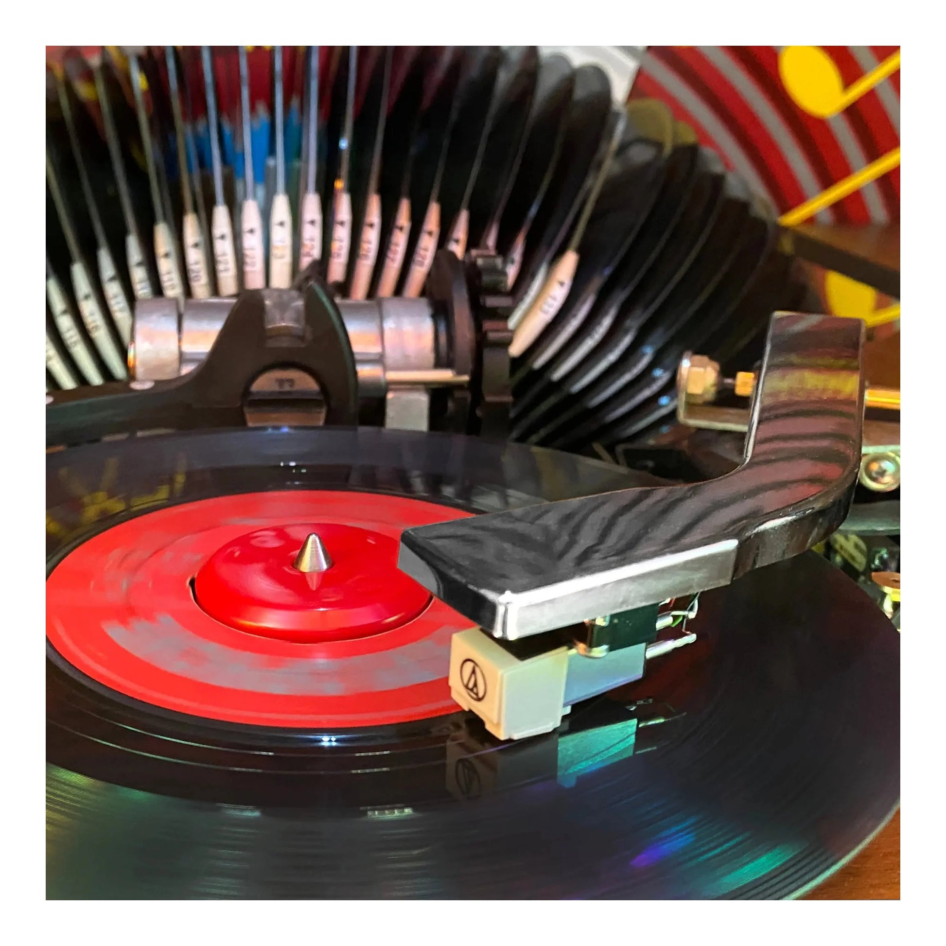 Close-up of a vinyl record player with a red record and stylus on a blurred background.