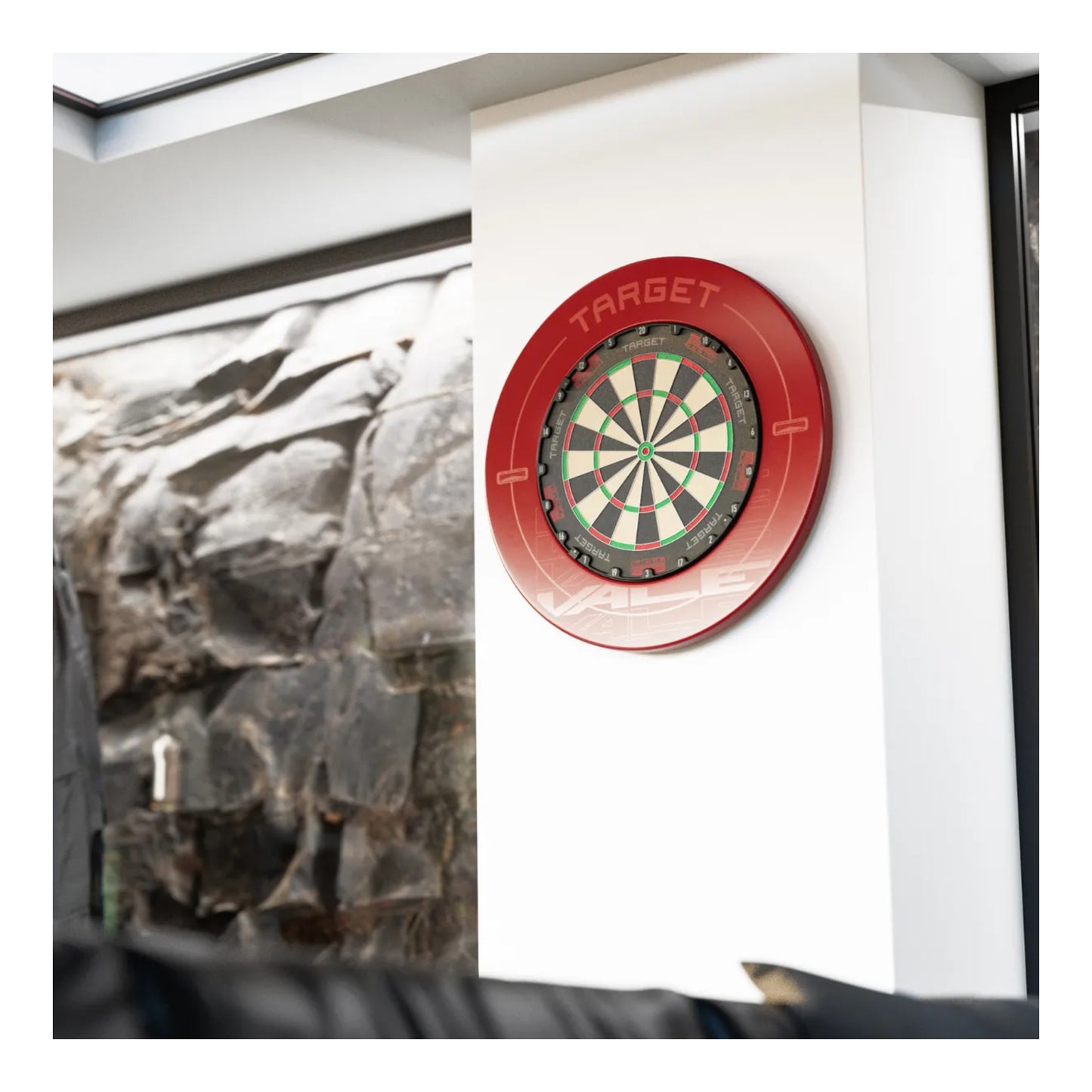 Target TOR Dartboard with red rim on a white wall next to a framed picture of rocks.