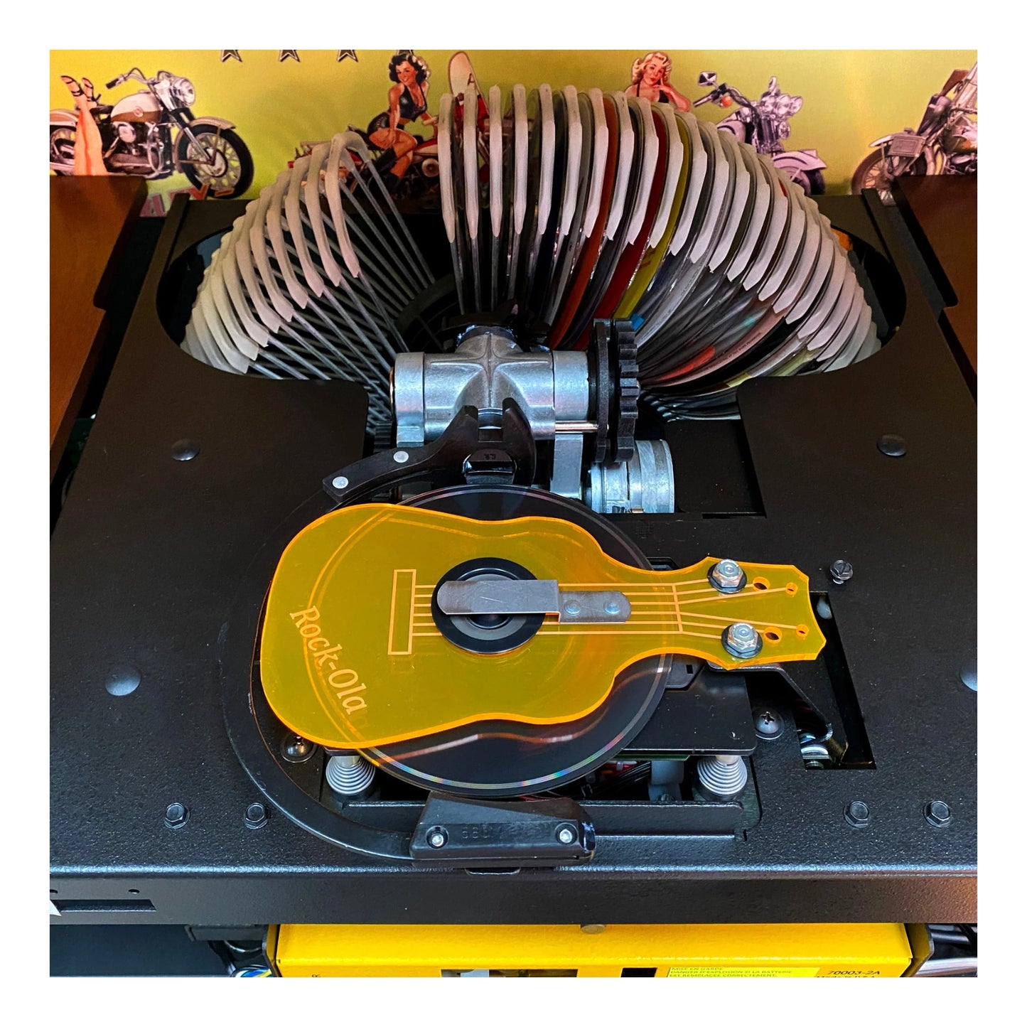 Close-up of a mechanical device with a guitar-shaped component on a yellow background.