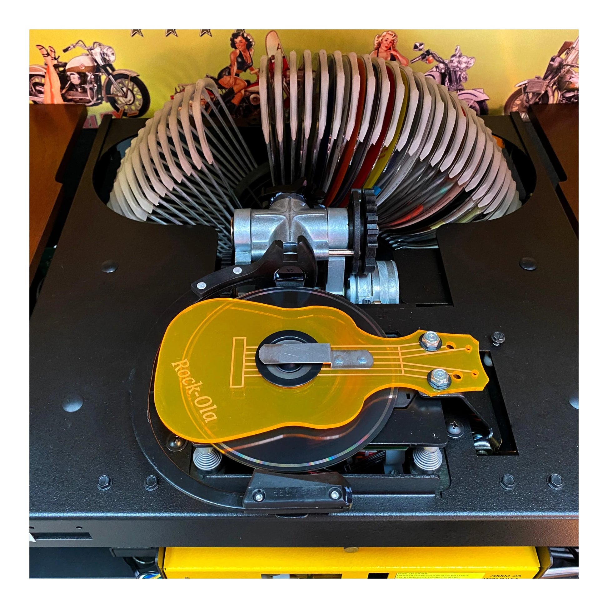 Close-up of a mechanical device with a guitar-shaped component on a yellow background.