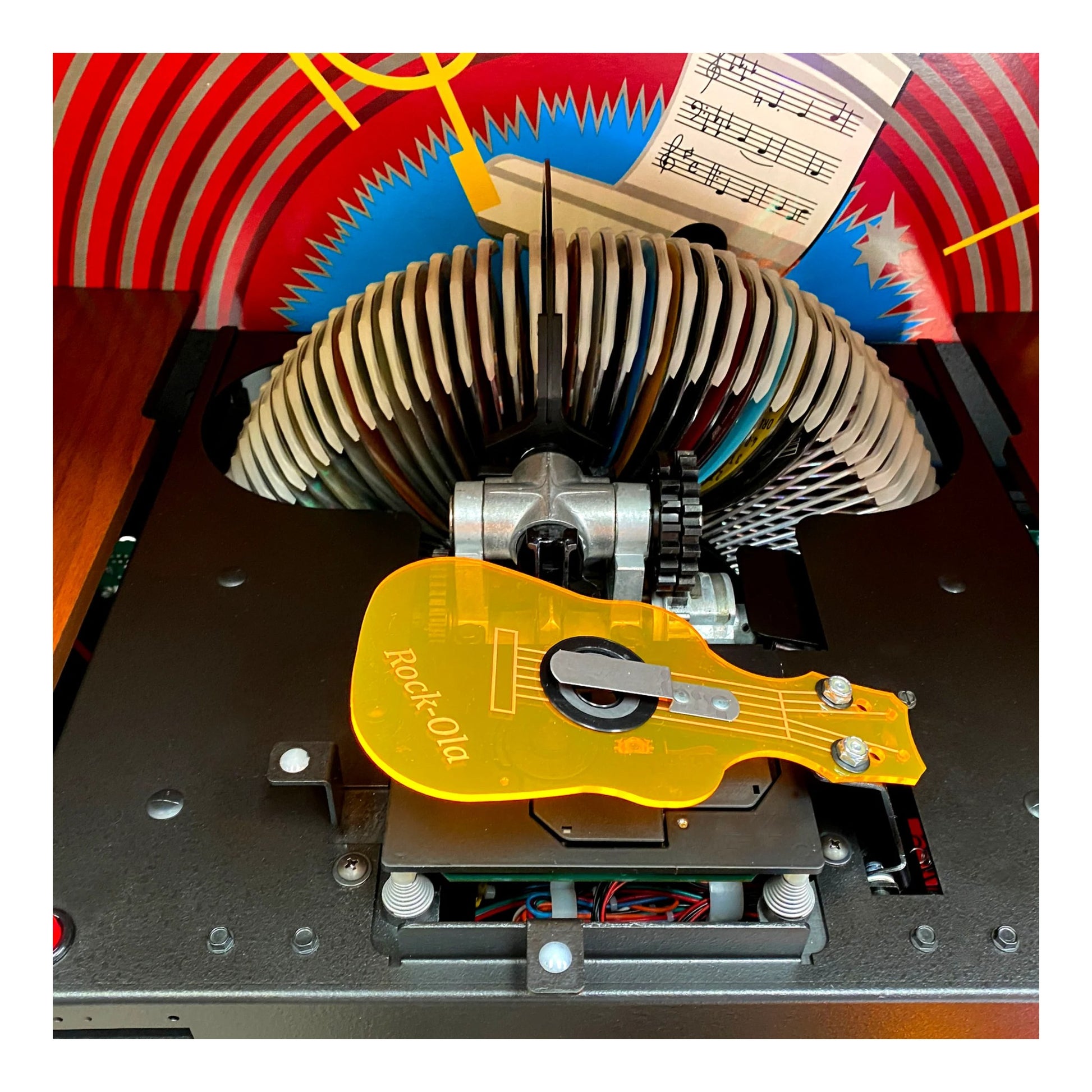 Close-up of a mechanical device with a yellow component labeled 'Rock-Ola' against a colorful abstract background.